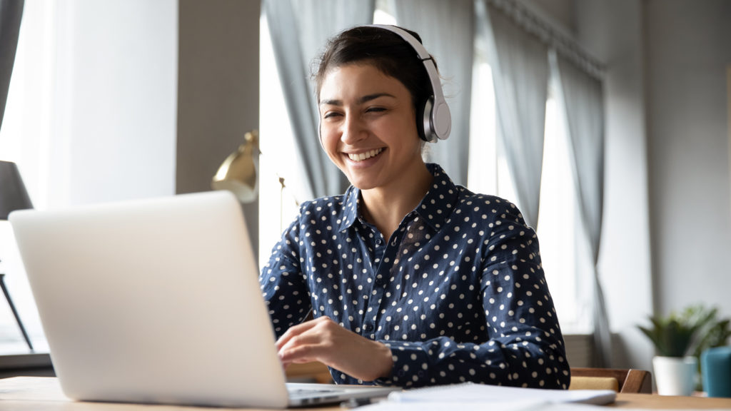 Smiling travel agent wearing headphones using laptop to access the WINGS Booking Platform through Sky Bird Travel & Tours, excited to learn about the best airline consolidator.