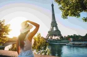 Woman in a white dress and sunhat stands by the Seine with the Eiffel Tower in the background at sunset/dusk. (Back view)